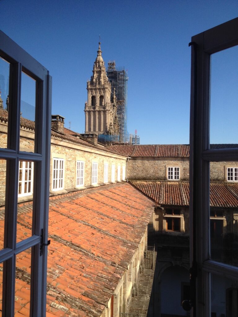 Blick aus dem weit geöffneten Fenster über die roten Ziegel Dächer vom einstigen königlichen Krankenhaus auf den Kirchturm der Kathedrale von Santiago de Compostela an einem sonnigen Wintertag